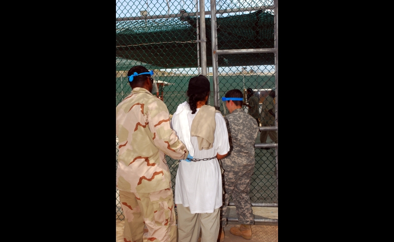 Photo by Navy Petty Officer 2nd Class Michael Billings - http://www.jtfgtmo.southcom.mil/photoarchive/2007/Sep07/featuredsep07.html. Licensed under Public Domain via Wikimedia Commons Guards escort a Guantanamo captive in chains to a recreational area